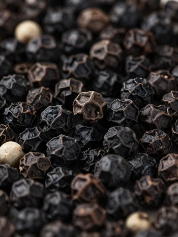 Fekete borsszemek és őrölt bors kerámia tálban és fa felületen