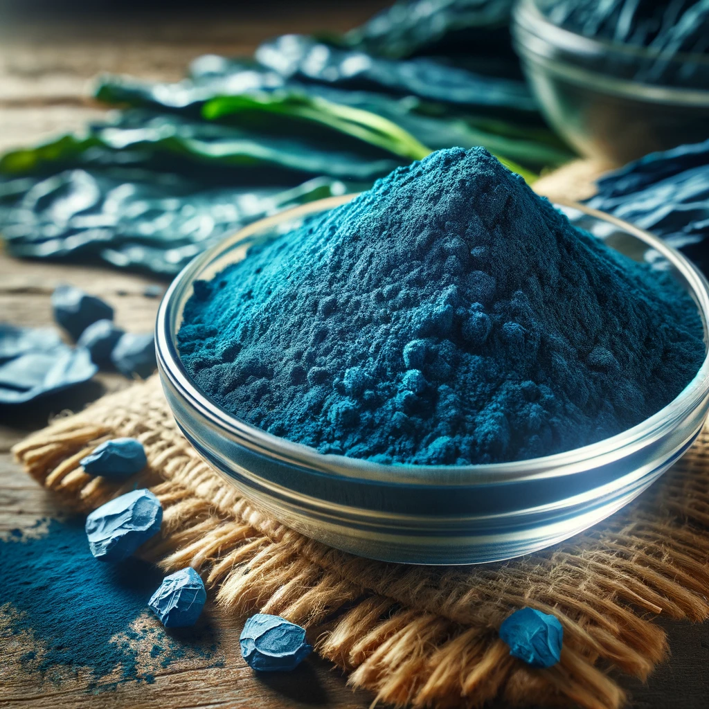 A képen kék spirulina por látható, élénk kék színben, egy kis üvegben elhelyezve, körülötte spirulina algák a természetes forrást hangsúlyozva.