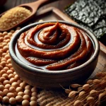 Miso paszta kis üvegben, gazdag barna színben, körülötte szója babok, szárított algák és rizs